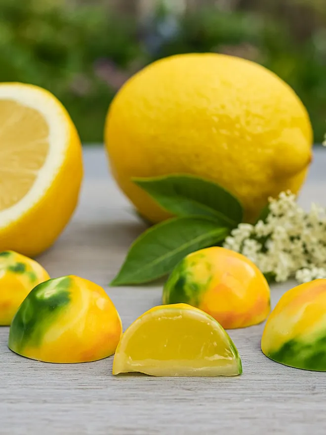 A lifestyle image of some white chocolates with lemons and elderflower in the background