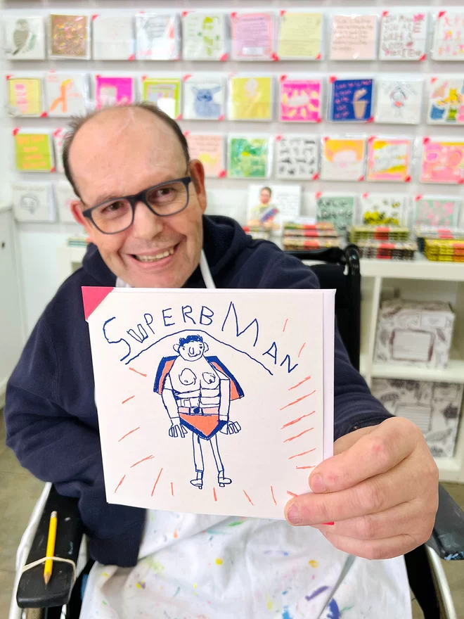 Artist holding the Superbman riso printed charity father's day card with a picture of a man in a cape