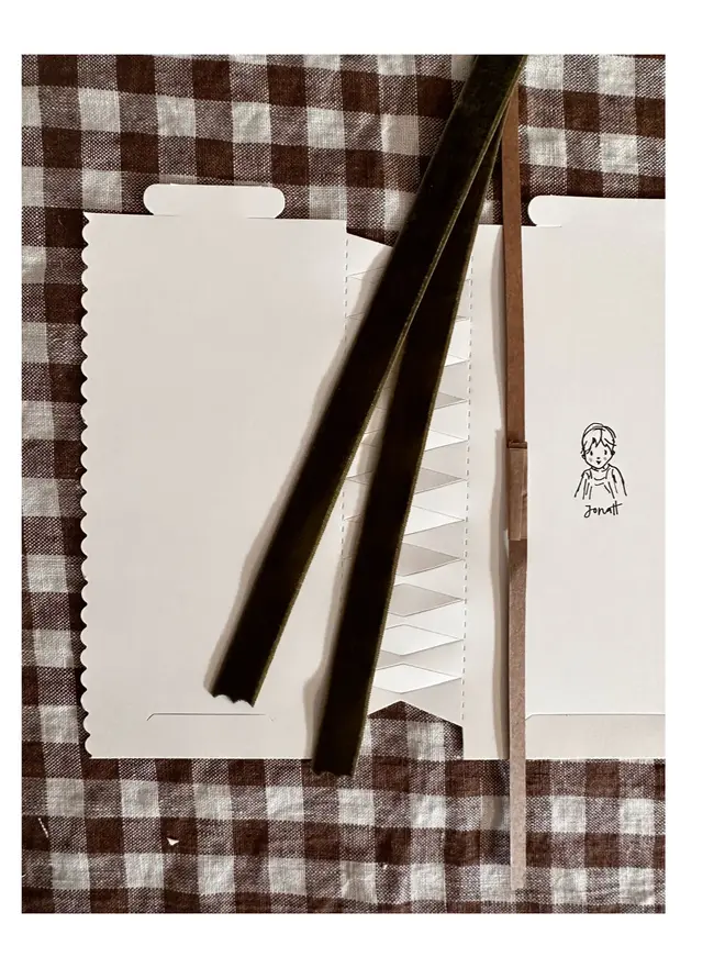 contents of cracker for make your own choice - white flat-laid cracker with bespoke cat illustration, velvet ribbon, and 'cracker snap' lying on white and brown gingham tablecloth