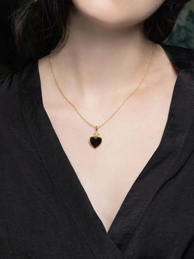 Model neckline wearing black enamel heart necklace on gold chain