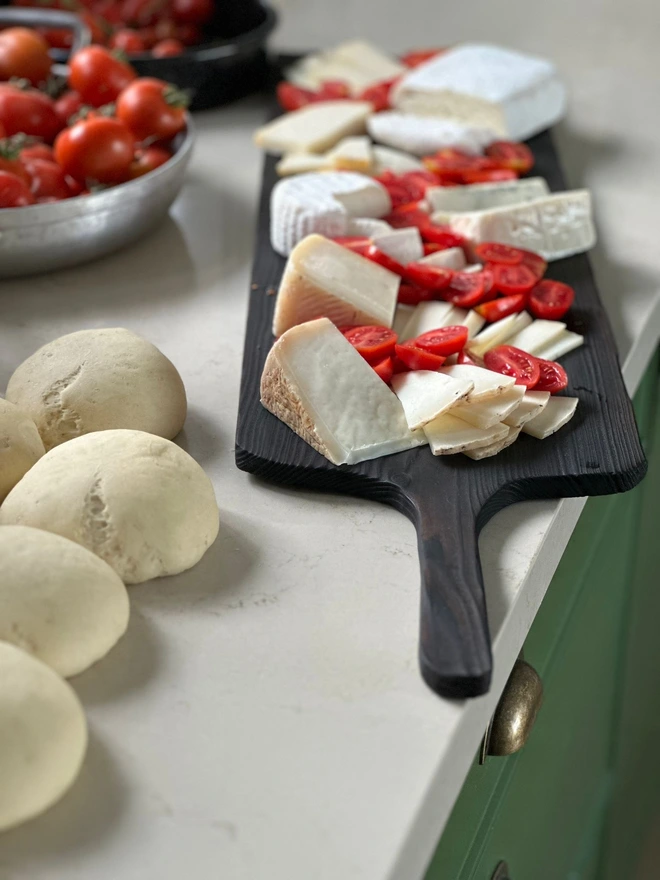 Long handled sharing board charred black with tomatoes and cheeses
