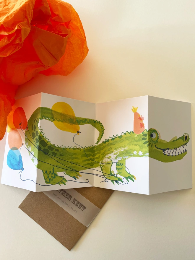 Esther Kent illustrated concertina greeting card showing a creen crocodile on a white background, with colourful balloons