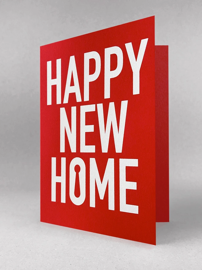 Happy New Home, screen printed in white ink on a red card. The card is on a grey background, slightly open.