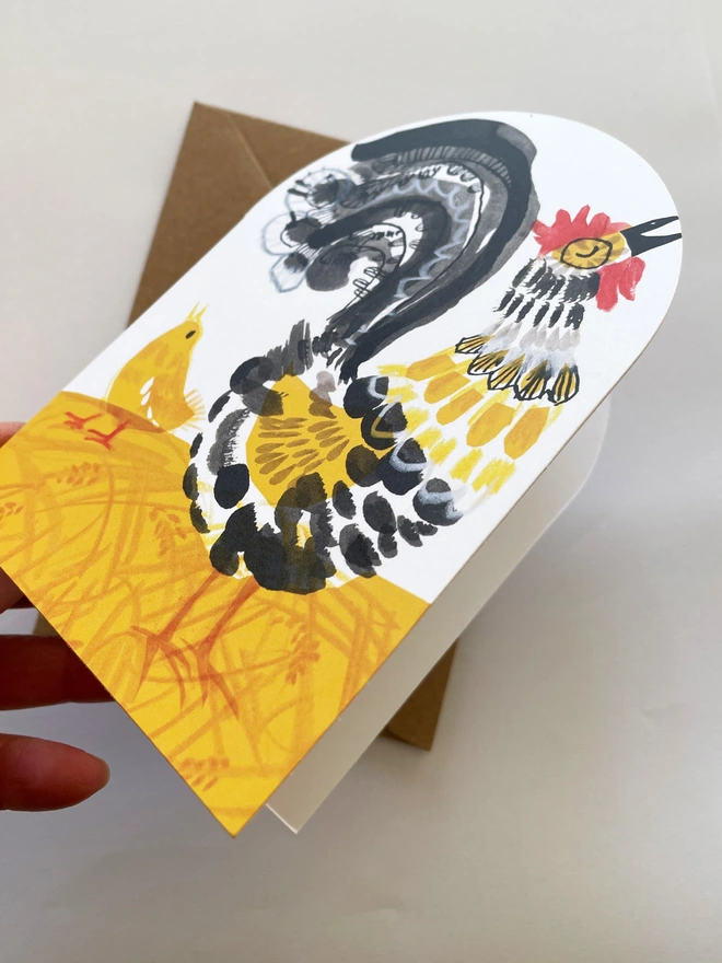 Esther Kent illustrated greeting card showing black, yellow and red stylised cockerel on an arch-shaped card