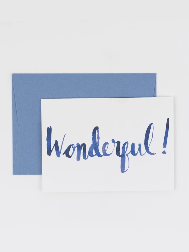 A greetings card featuring the word "Wonderful!" in large navy blue brush lettered letters. It is photographed with a pale blue envelope. 
