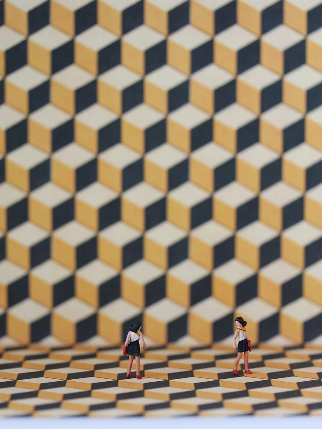 Miniature scene in an artbox showing two tiny women glancing at each other, set against a geometric backdrop (close up). 