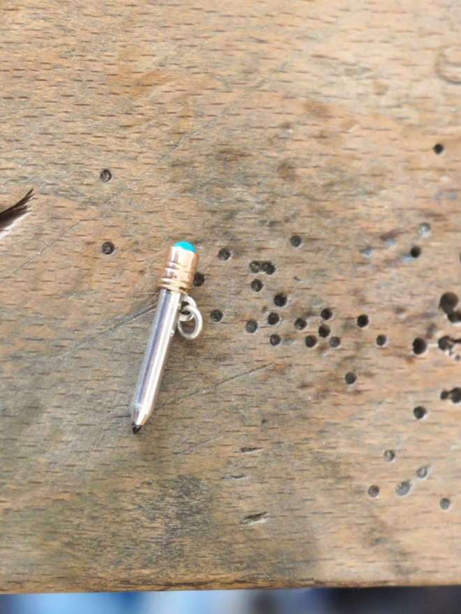 Dinky Pencil Charm. A pencil charm on a piece of wood.