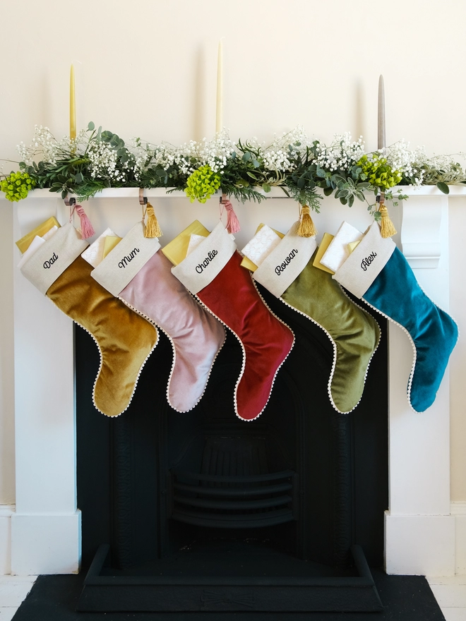Five luxury velvet christams stockings with pom pom trim hung from the mantelpiece.