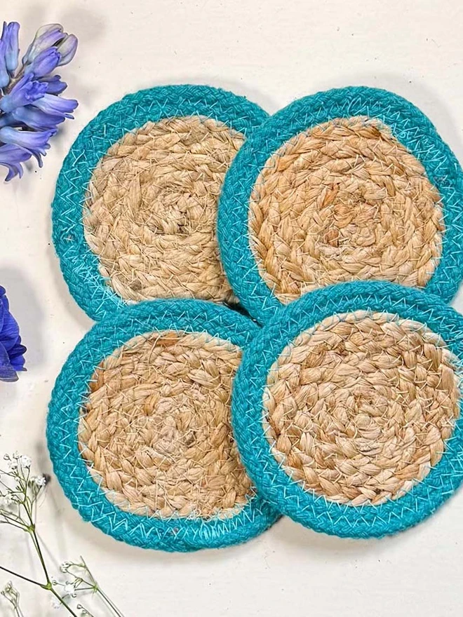 Close up seagrass coaster with teal rings, shown on a light surface with purple flowers. 