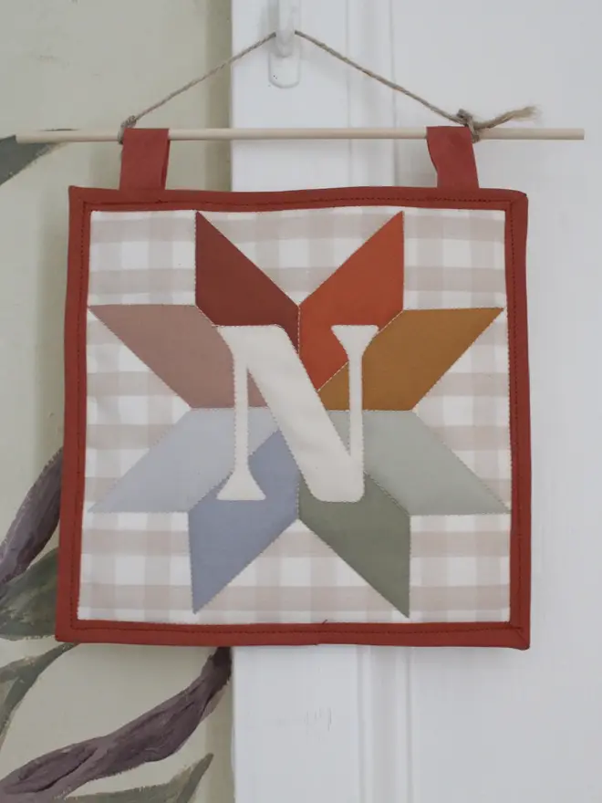 personalised initial quilt hanging. a hand-sewn hanging quilt with a star design in the centre, alongside the initial 'N'.