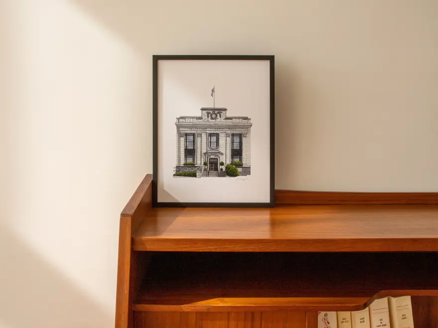Islington Town Hall Giclée Print (Unframed), a print of a town hall sitting in a black frame on a wooden surface against a plain backdrop. 
