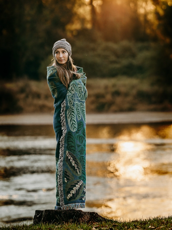 Indoor Jungle Window rug by Arcana seen wrapped around a person standing next to a river.