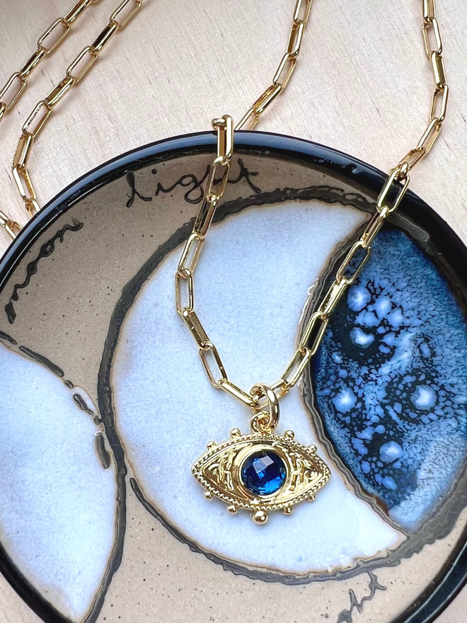 Blue evil eye charm with gold paperclip necklace on celestial dish