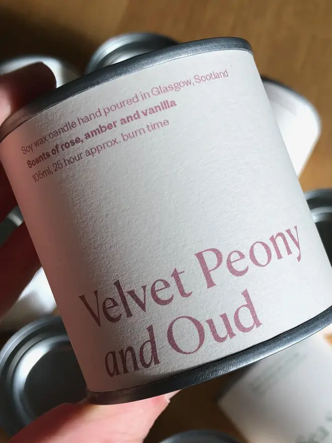 Velvet Peony & Oud Candle, held in a hand against a white background. 