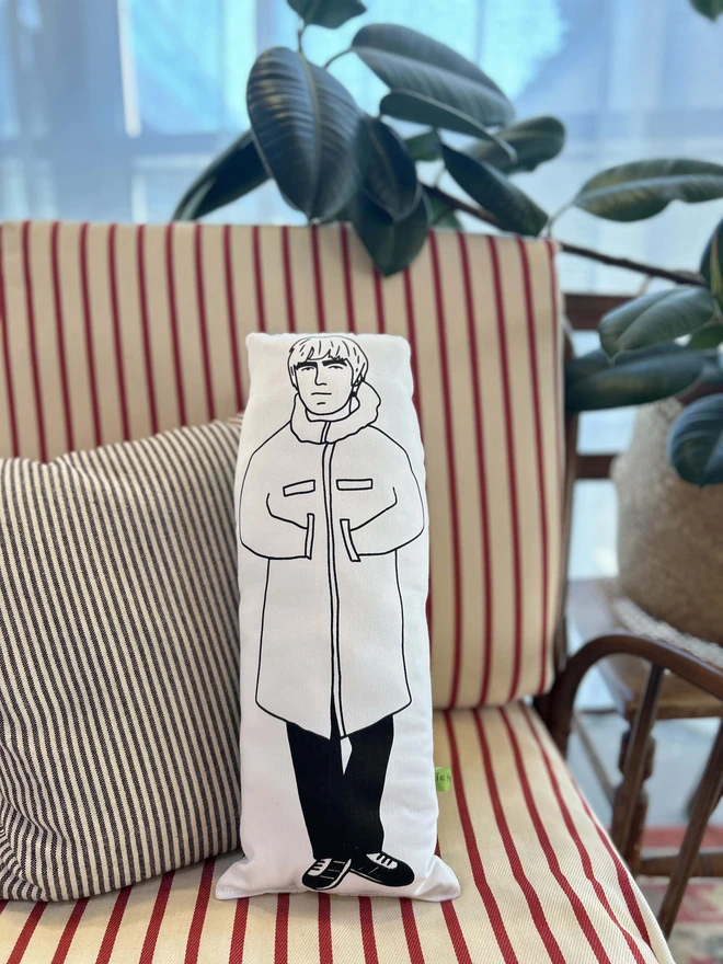 Black and white illustrated screen printed cushion of Oasis band member Liam Gallagher. The cushion sits on a striped sofa.