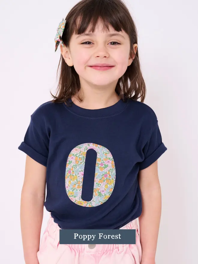a 5 year old girl wearing a personalised kids personalised navy t-shirt with an initial cut from poppy forest  liberty floral print on the front
