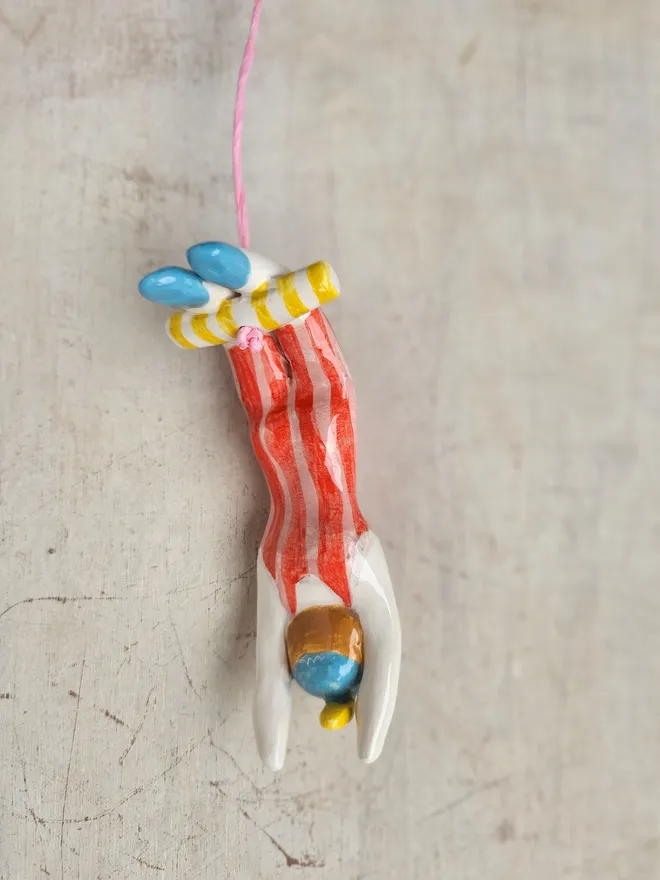 female acrobat hanging upside down in a red and pink stripe suit, back view