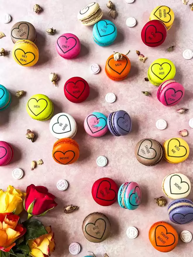 colourful valentine's day macarons, decorated like conversation love heart candy on a pink background with colourful roses