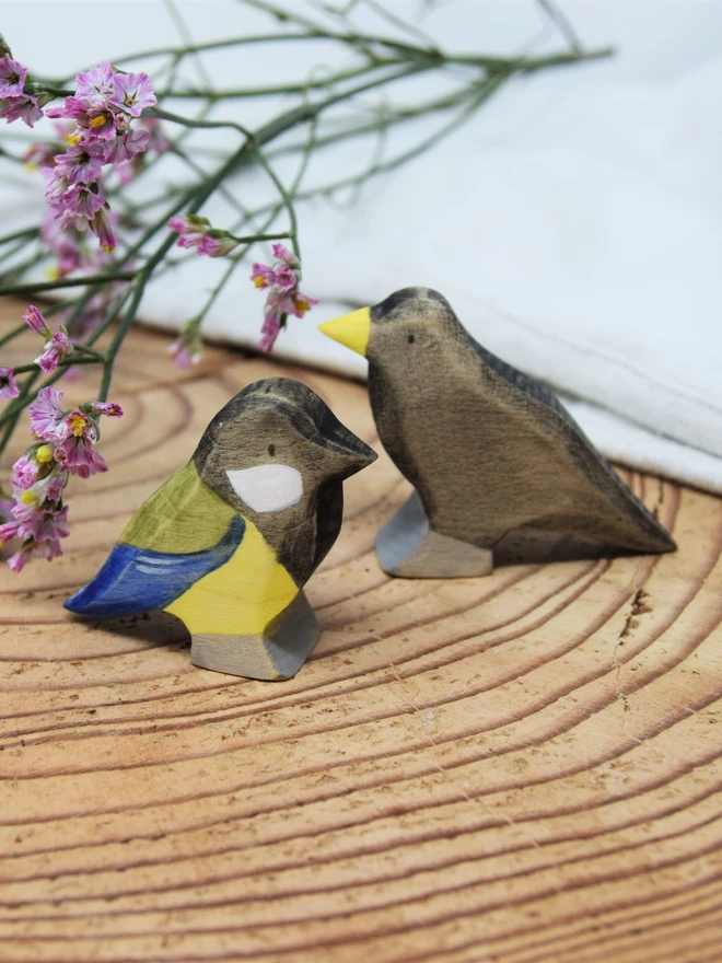 wooden toy garden birds, blackbird and great tit sat on log with dried flowers