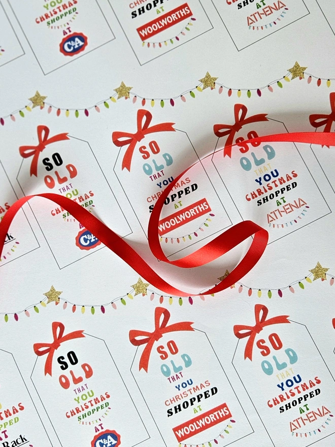 A close up photograph of the wrapping paper with tags that say so old you Christmas shopped at Woolworths, Tie Rack, C&A, Athena.