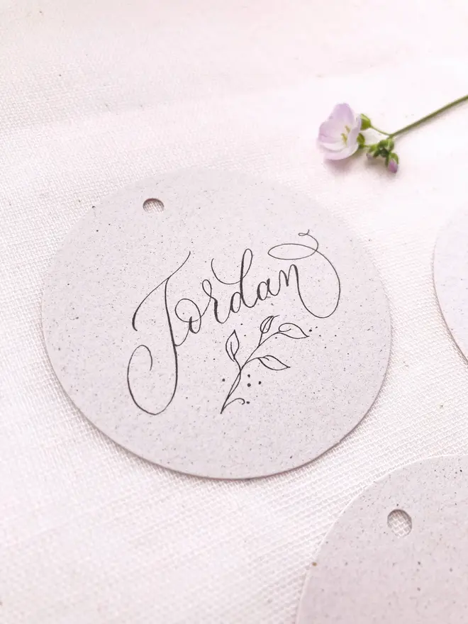 circular calligraphy wedding place cards. white circular place card with black calligraphy.