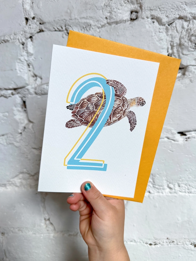 a white card with a big blue number 2 and a turtle illustration with a bright yellow envelope
