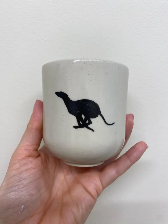 Black Greyhound Handmade Ceramic Coffee Cup, a coffee cup with a black greyhound design held against a white backdrop. 