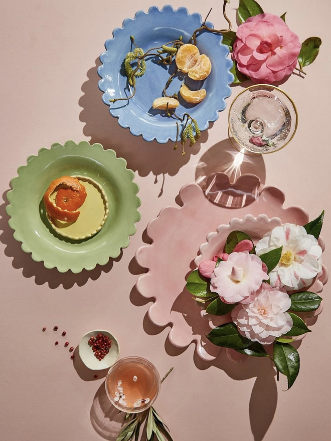 a sage green and a periwinkle blue shallow bowls shown on a styled image with camellias, stemware and a large pink serving platter