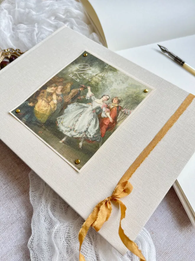 The Dance wedding guest book, linen cloth covered book with 18th century romantic scene of a couple dancing and finished with gold ribbon