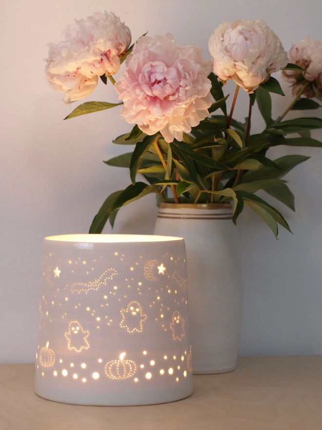 A ceramic cylindrical lamp, made from porcelain, featuring a design pierced into the clay of ghosts, pumpkins bats and stars.