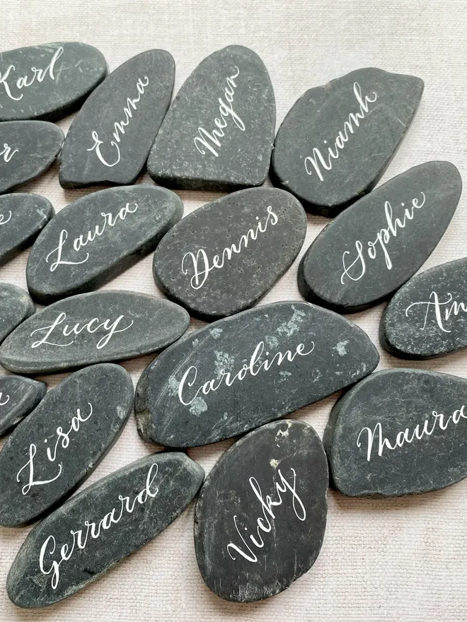 Granite slice place cards with your guest names hand scripted in white ink using a dip pen. The granite slices are flat and smooth and of varying size and shape