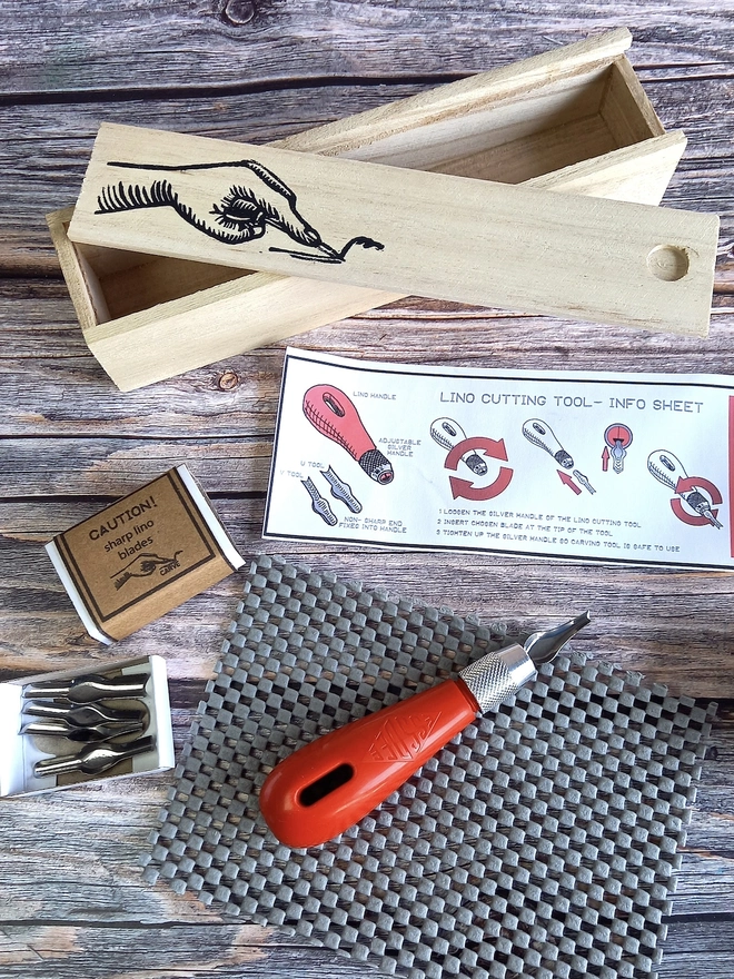 Lino Carving Printing Tool Kit In Presentation Box, carving utensils and instruction sheet unpacked on a table next to wooden presentation box. 