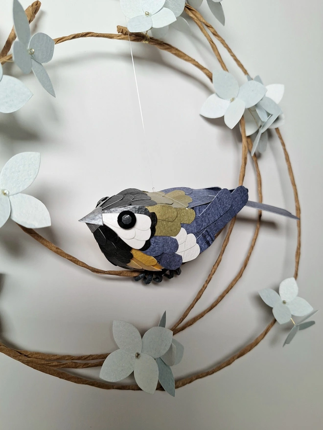 close up of a great tit garden bird sculpture, perched on a wreath adorned with baby blue hydrangea blooms