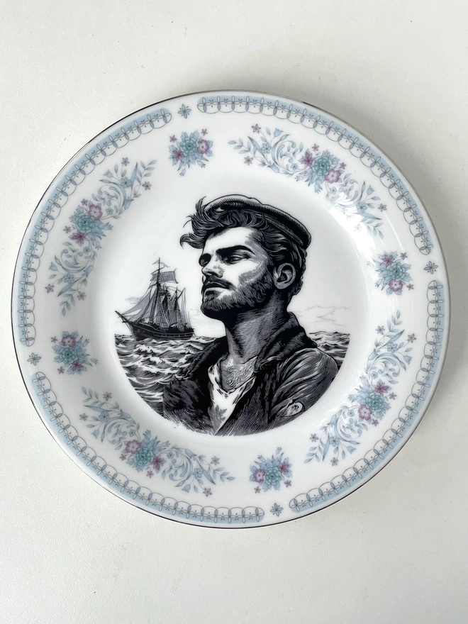 a white plate with a printed vintage illustration of a sailor man in the middle with the ocean and his ship behind him