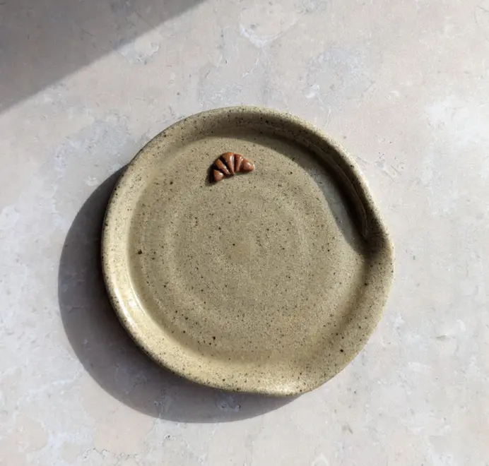 Croissant stoneware spoon rest in biscuit glaze against a grey marble background.