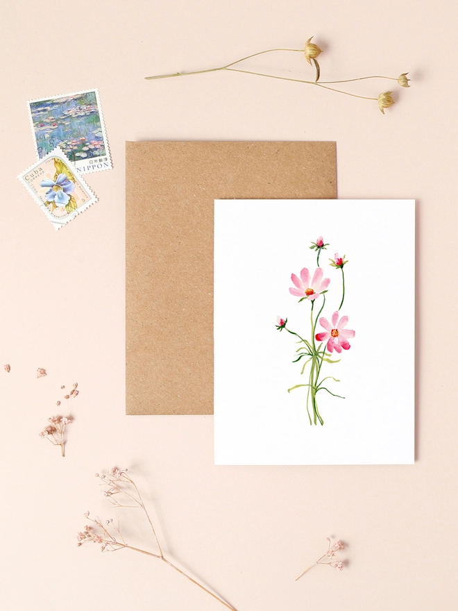 A delicate illustration of a single cosmos flower with soft pink petals and a yellow center, set against a muted background. The flower's gentle curves and fine details capture its natural beauty. The card is left blank inside, providing space for a personal message. Printed on thick, textured FSC-certified board, this eco-friendly mini card measures 90mm x 120mm, making it a charming choice for various occasions.