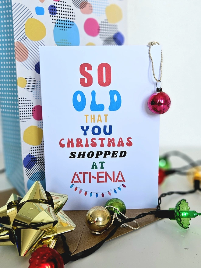 A photograph of the front of a humorous A6 greeting card illustrated using brightly coloured text and the retro shop logo. The text says so old you Christmas shopped at Athena