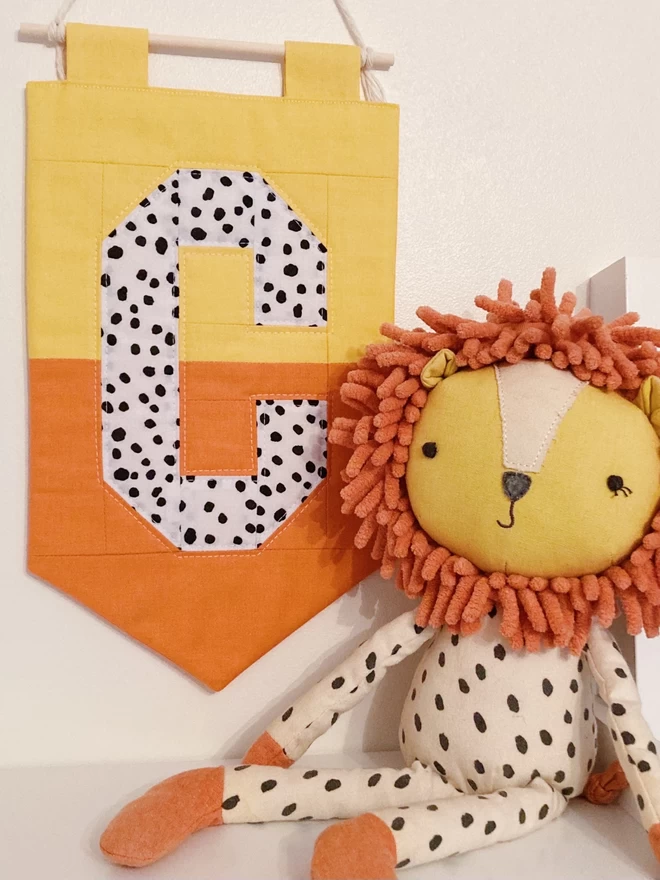 Cooper and Fred colour block quilted wall hanging with yellow and orange background and spotty letter 'C'.