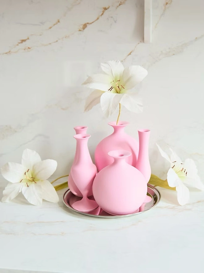 collection of various shaped pink vases with white flowers all on a tray
