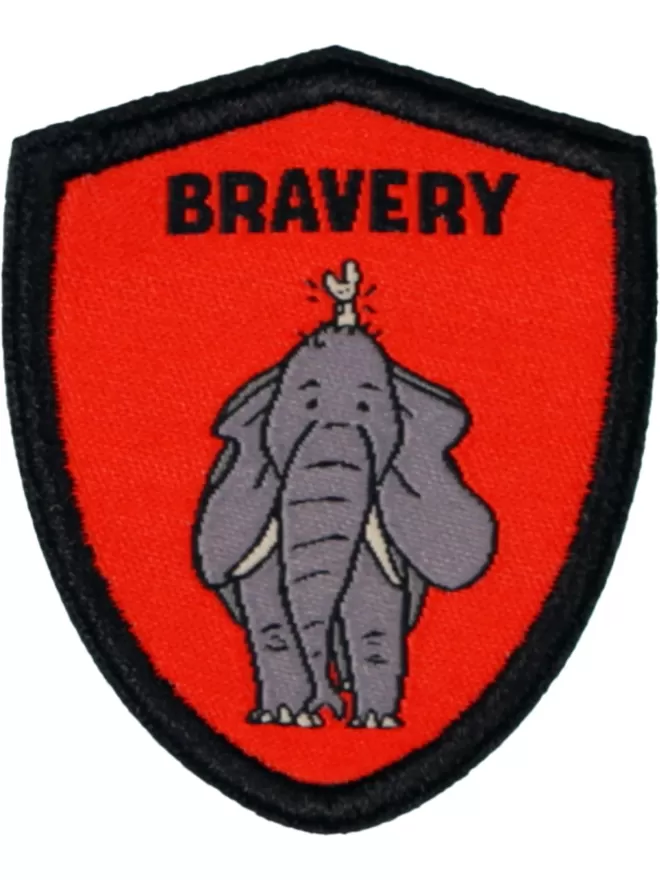 A red badge shaped patch with bravery written in bold letters at the top. In the centre is an elephant with a small mouse seated on its head.
