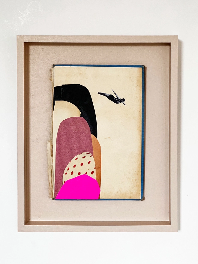 A paper collage on an old book cover within a painted pale pink frame. Featuring a female swimmer diving off a group of colourful tall rocks.