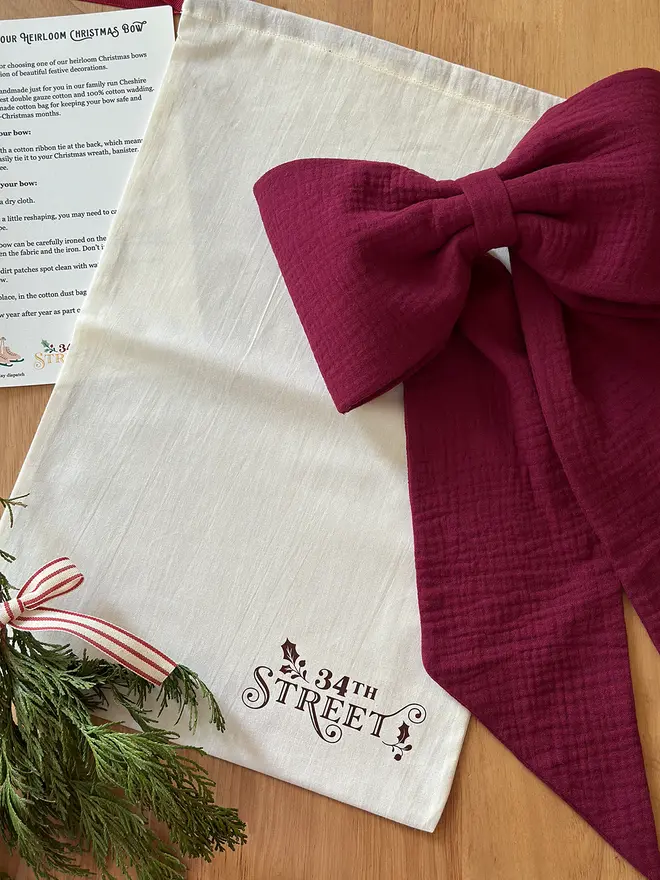 A cotton bag with the 34th Street logo on lays on a wooden desk with a handmade Christmas bow beside it.