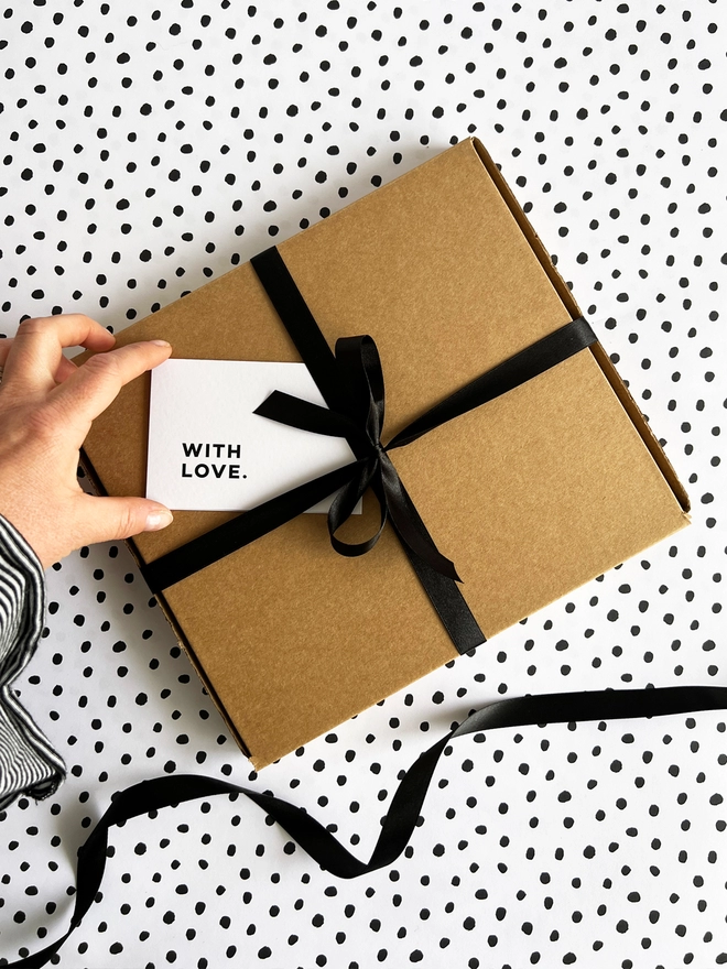 Lady removing the 'with love' notecard from the brown gift box tied up with a black ribbon. 