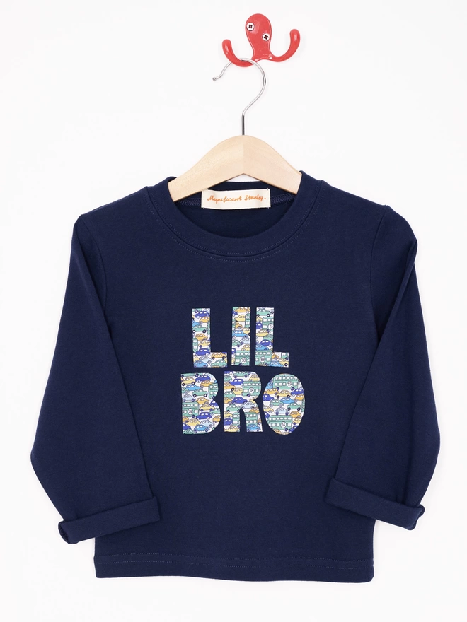 Lil Bro appliquéd on a long sleeve navy cotton t-shirt in vintage car print Liberty print, hanging on a hanger.