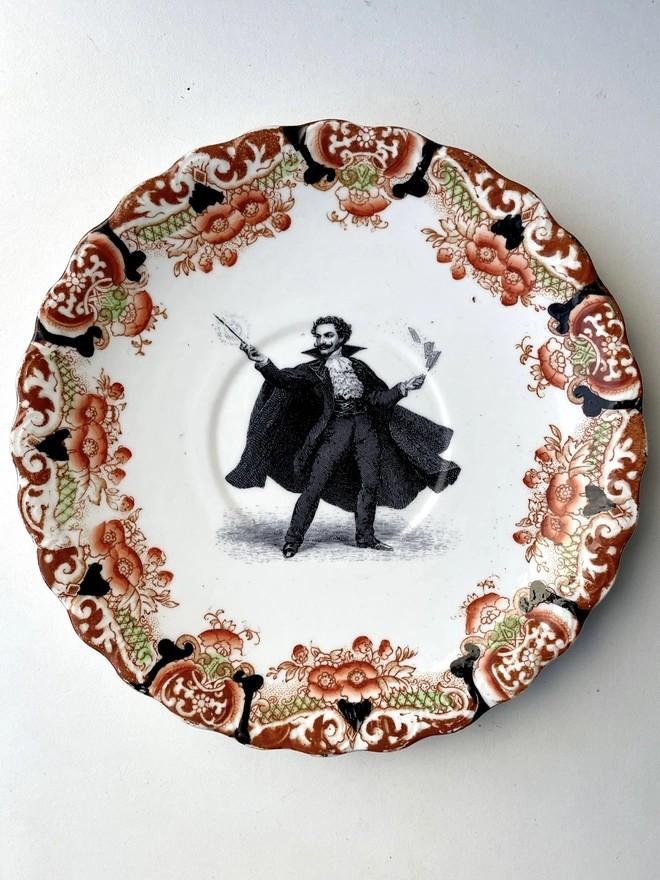 a vintage ornate plate in the centre i have printed a vintage black and white illustration of a dramatic magician cape wearing moustache casting spells with his wand