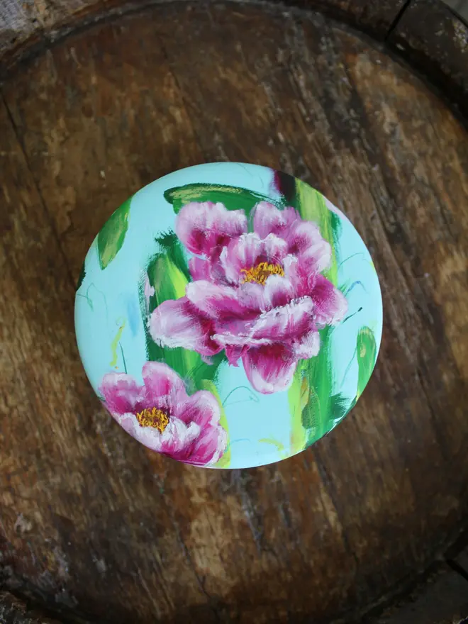 A beautifully hand painted floral ceramic round box background painted in a pale blue adorned in vibrant pink and white peony flowers.