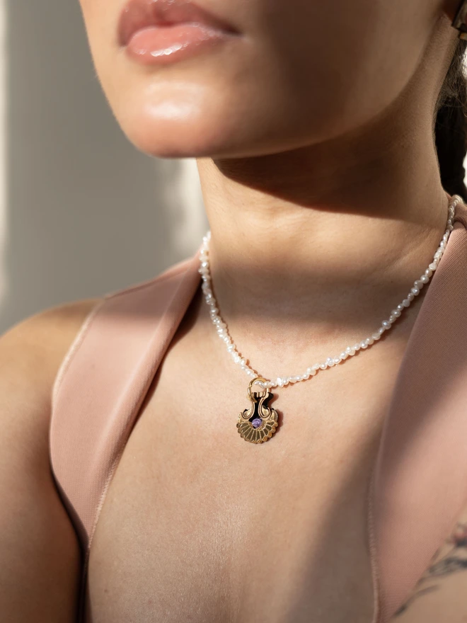 Pearl necklace with a shell shaped gold pendant & gemstone on a womans neck