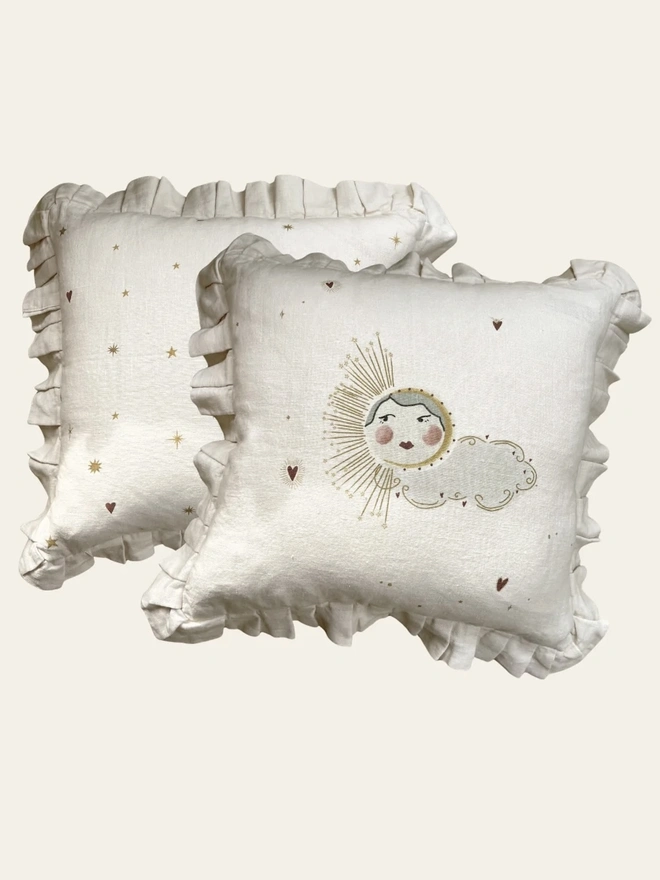 'Love Sun' Linen Ruffled Cushion Cover, a linen cushion with a sun and cloud motif on it sitting on a plain surface. 