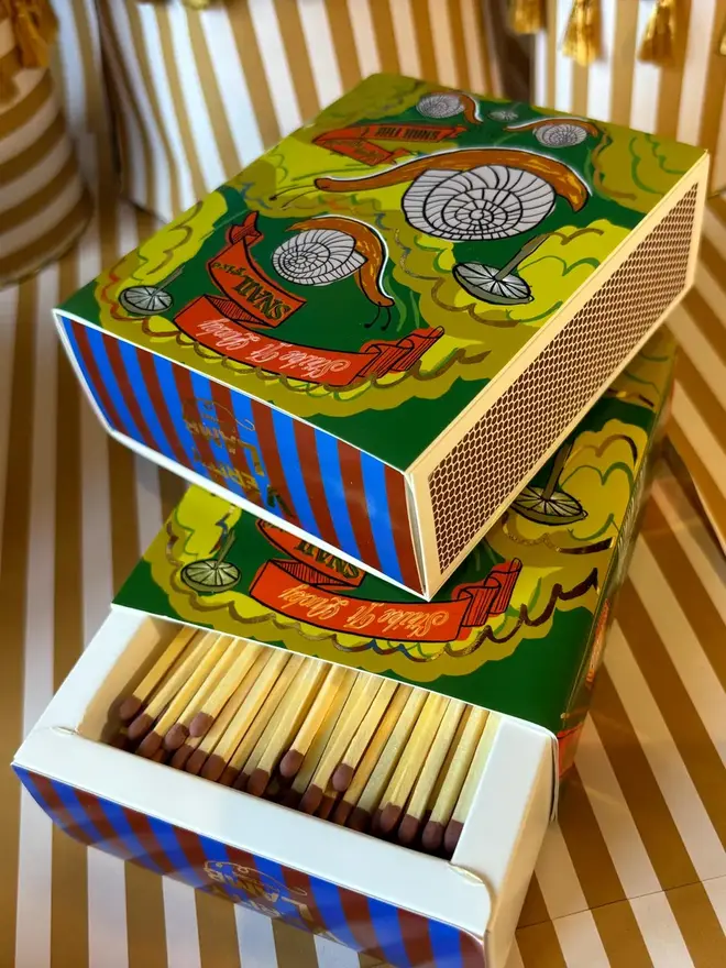 Snail Matchbox, a snail matchbox with a green design sitting on a decorated surface accompanied by other accessories.