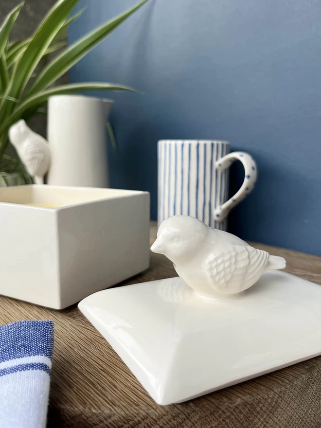 A close up handmade butter dish pot lid showing the textured feather details of its bird handle.